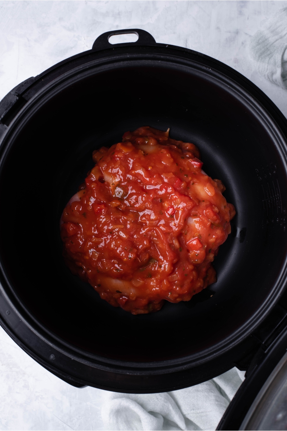 Slow cooker filled with raw chicken breasts that have been covered in salsa.