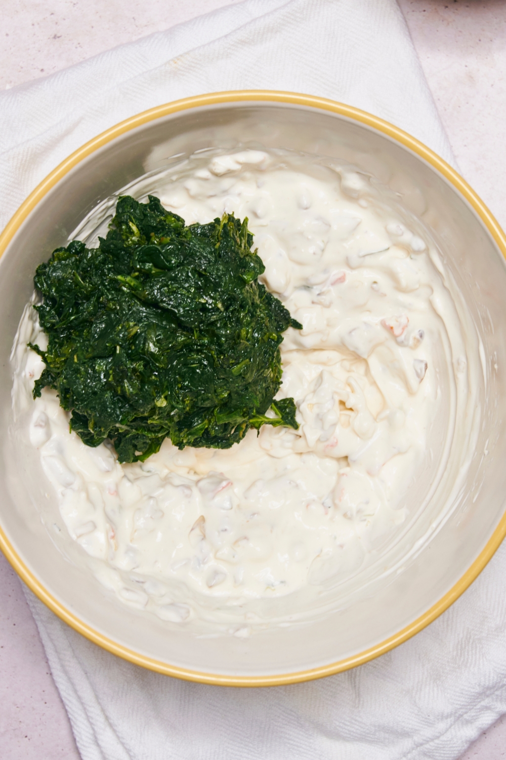 A bowl with the cream cheese, sour cream, knorr vegetable dip seasonings, and chopped water chestnuts mixed. Spinach has just been added to the bowl.