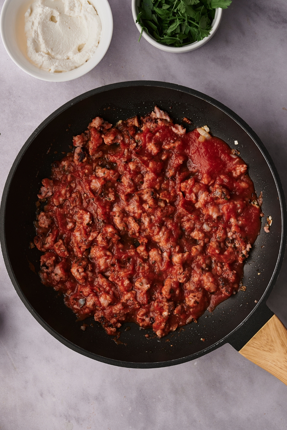 A skillet with cooked sausage, Italian seasonings, and tomato sauce.
