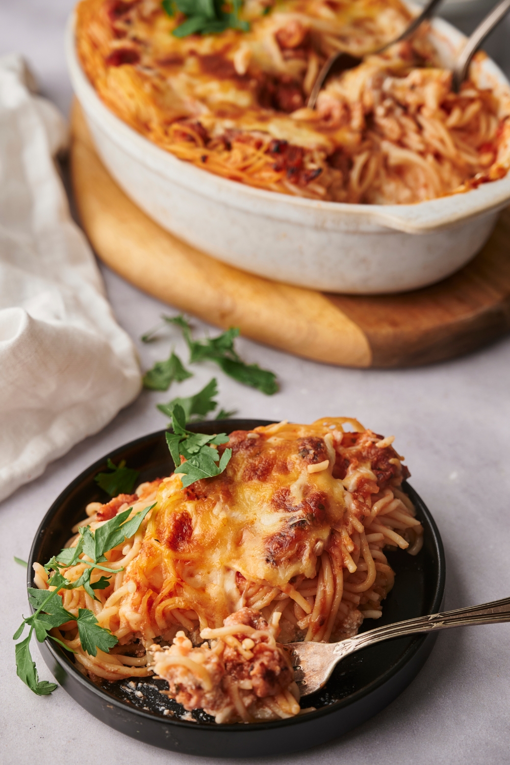 A small plate with a serving of spaghetti casserole. The remaining casserole is in a baking dish in the background.