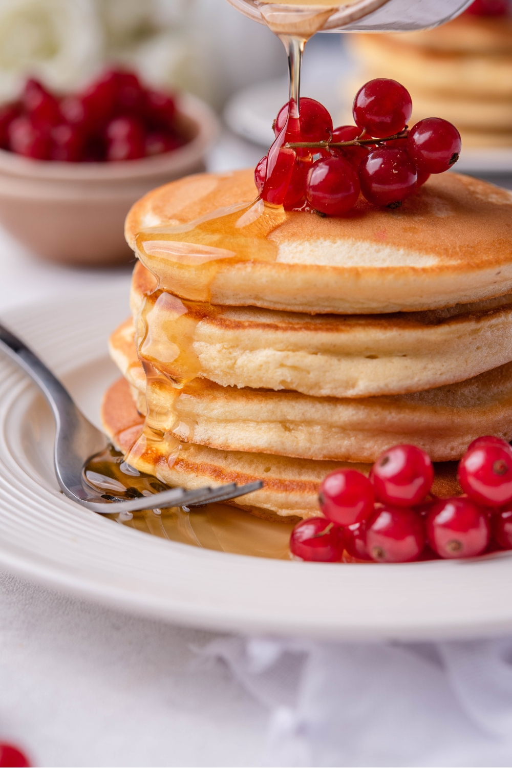 A stack of pancakes topped with fresh berries. Fresh syrup is being poured over the stack.