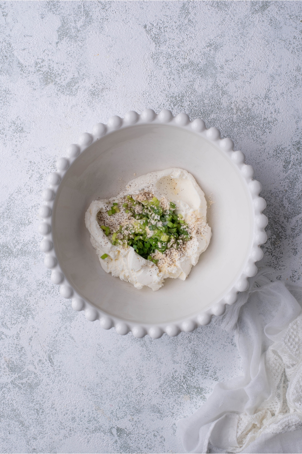 A decorative white bowl filled with cream cheese, green onion, and spices.