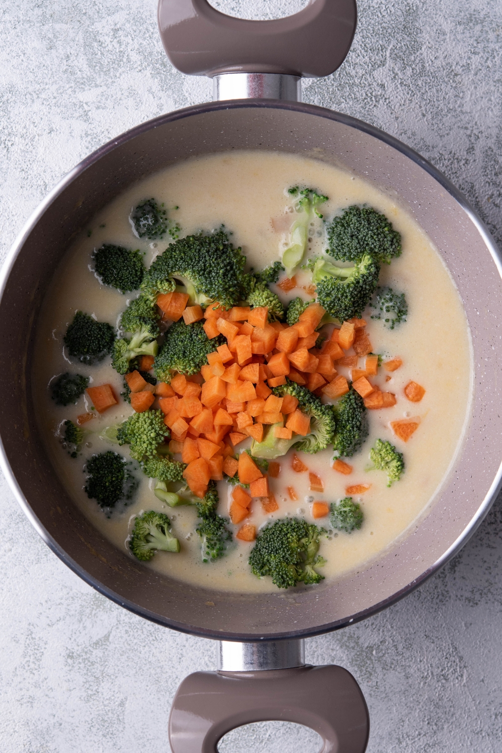 A deep pot with creamy broth and chopped broccoli and carrots.