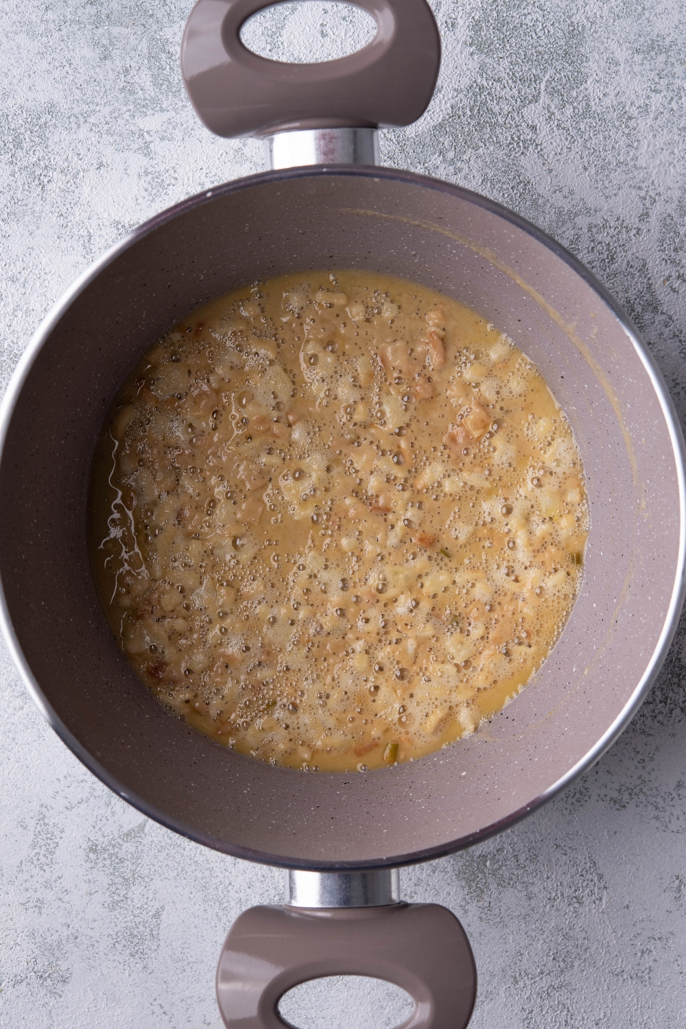 A deep pot with cooked onions in butter. Flour has been added to create a light tan color.