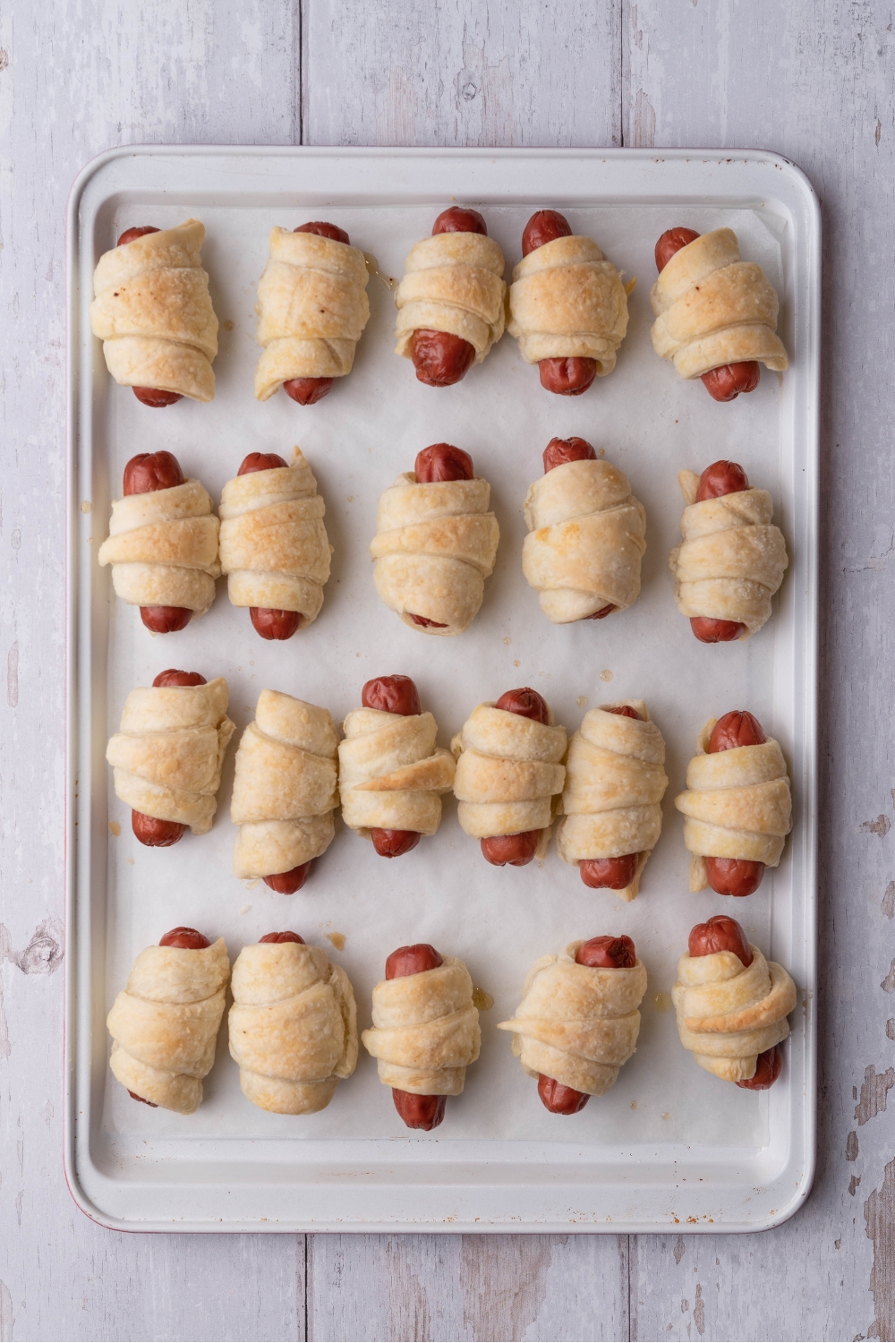 Pigs in a blanket evenly spaced on a baking sheet lined with parchment paper.