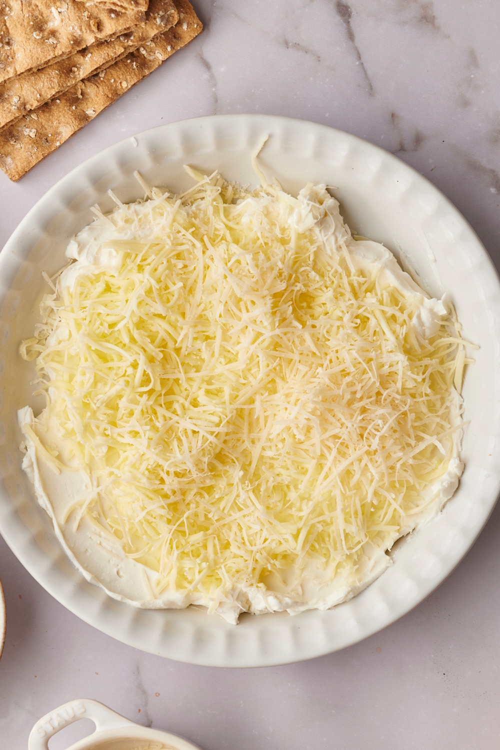 A pie dish with cream cheese and shredded cheese layers.