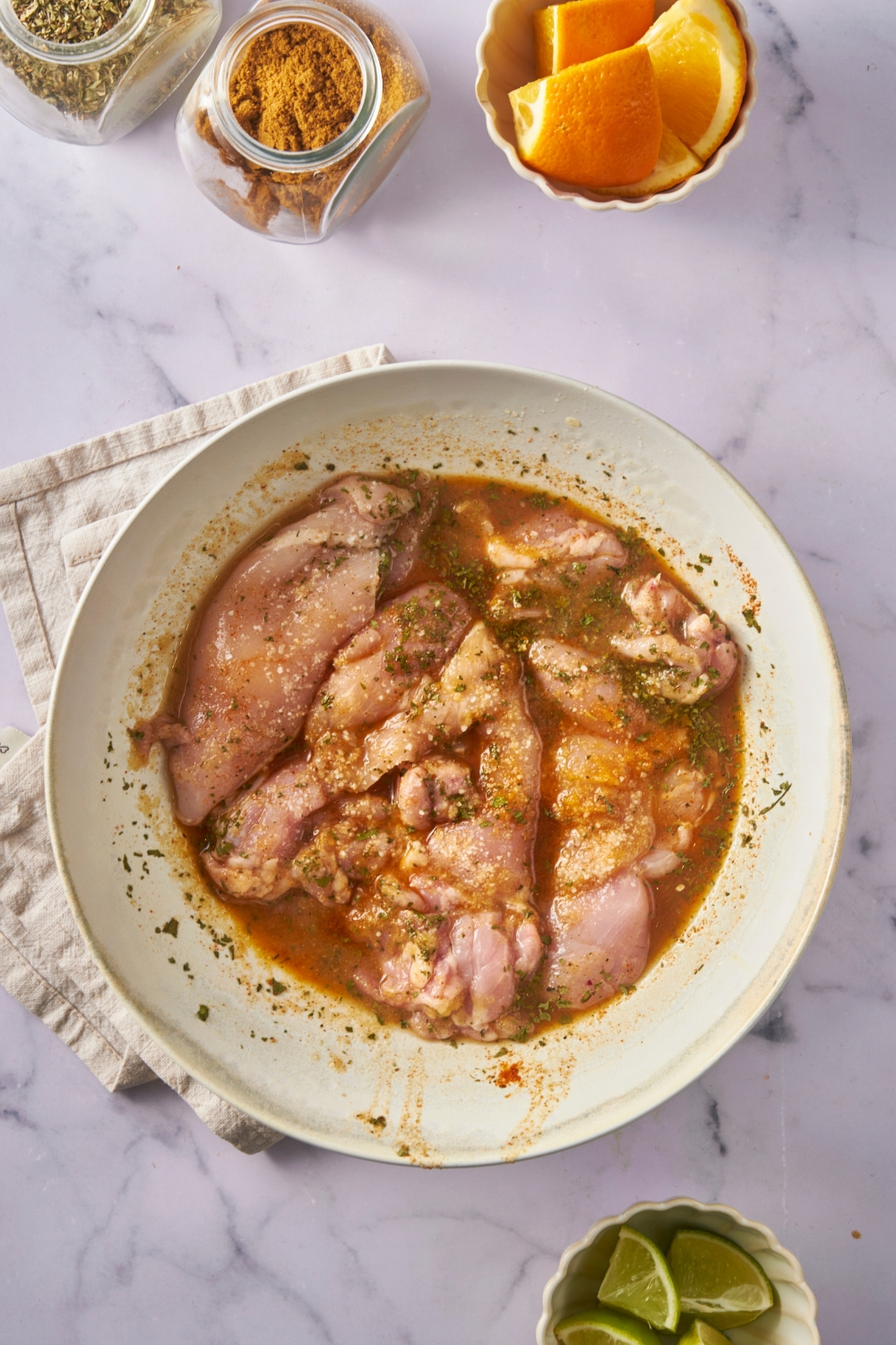A large mixing bowl filled with raw chicken in a citrus marinade.