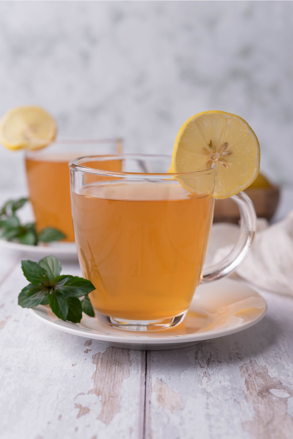 Two clear mugs with medicine ball tea in it and slices of lemon to garnish.