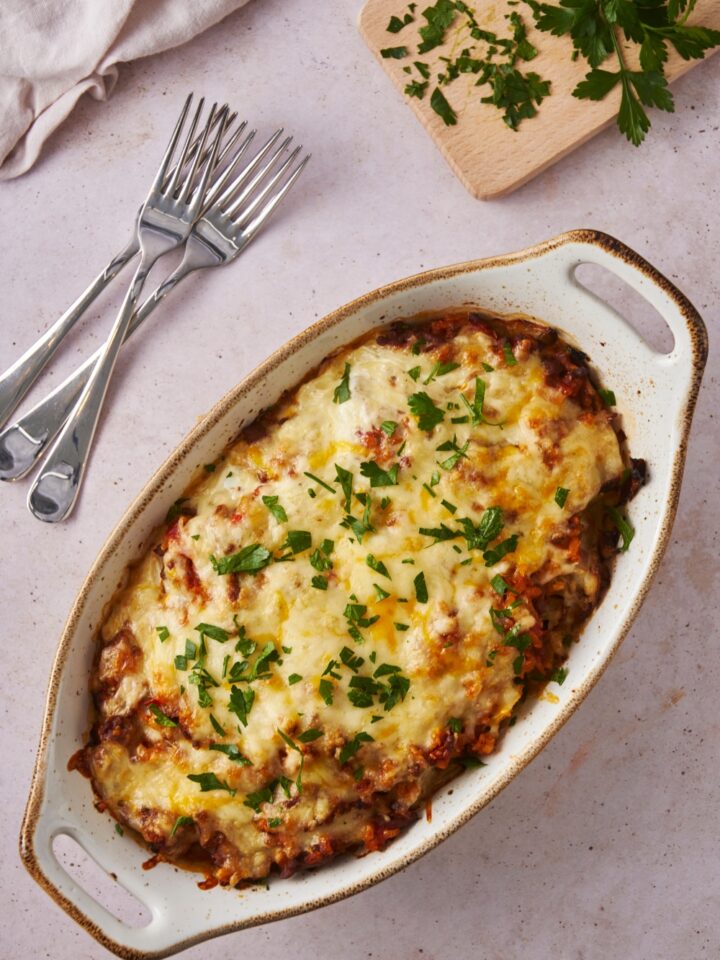 Cabbage roll casserole covered with melted cheese and fresh herbs, with three forks piled next to the casserole.
