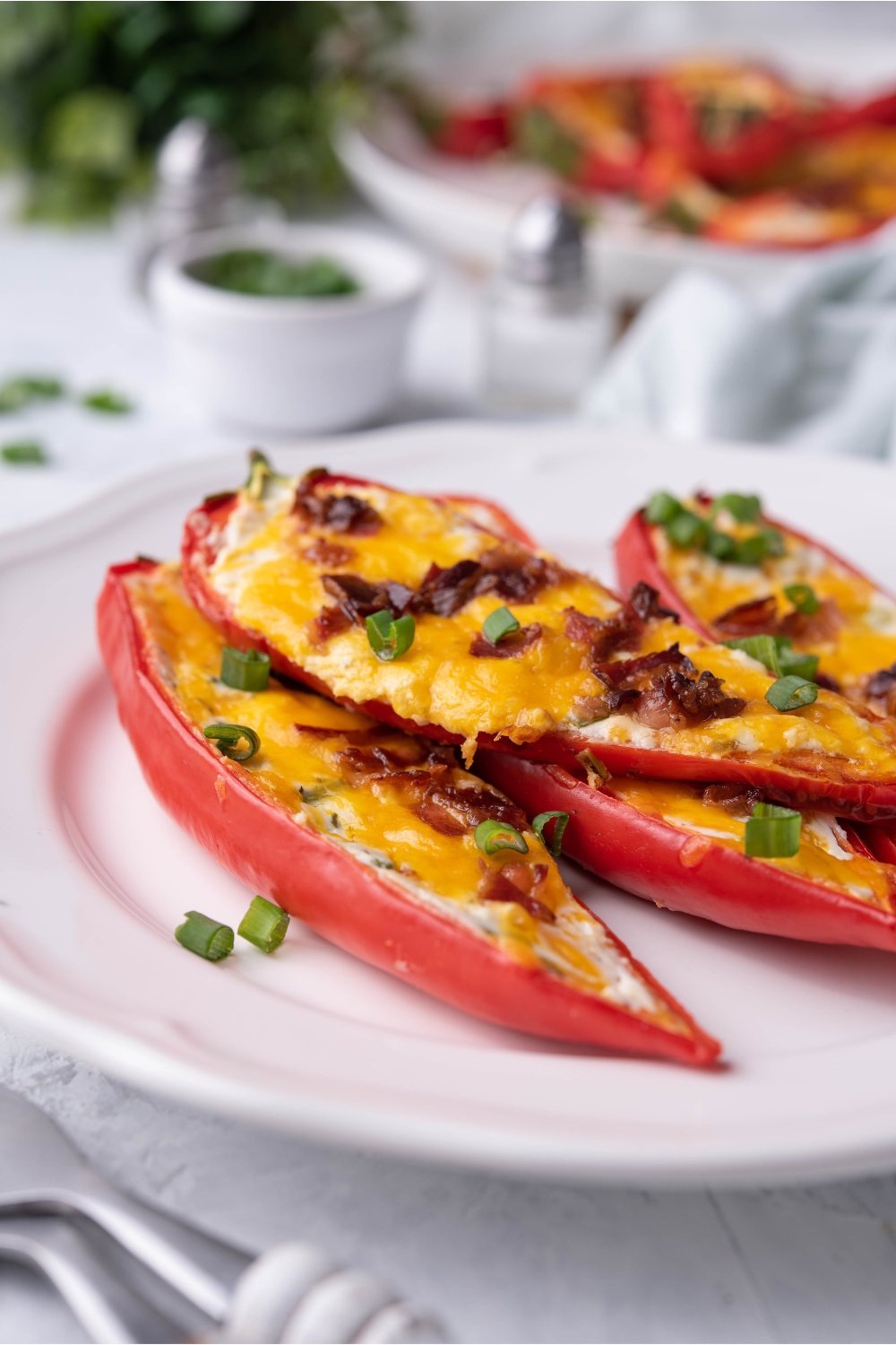 Four cream cheese stuffed peppers topped with sliced green onions piled on top of each other on a white plate.