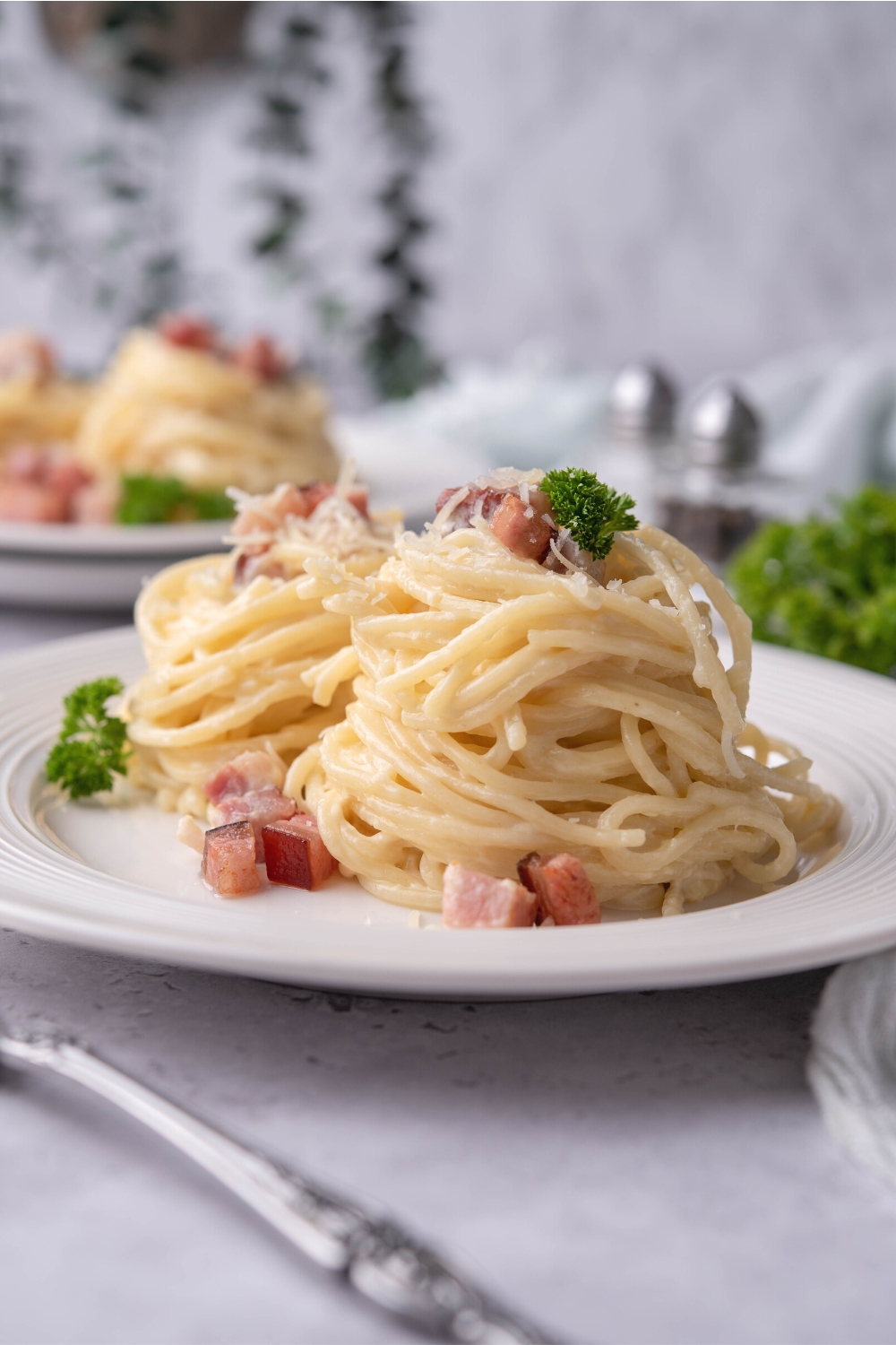 A mound of spaghetti noodles with diced pancetta and Parmesan cheese on top of a white plate.