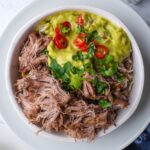 Barbacoa and guacamole with diced tomatoes on top in a bowl that is filled with rice.
