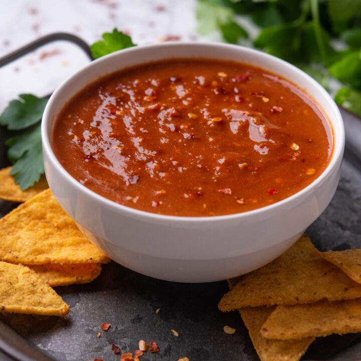 A bowl with chipotle hot salsa on a tray surrounded by tortilla chips.