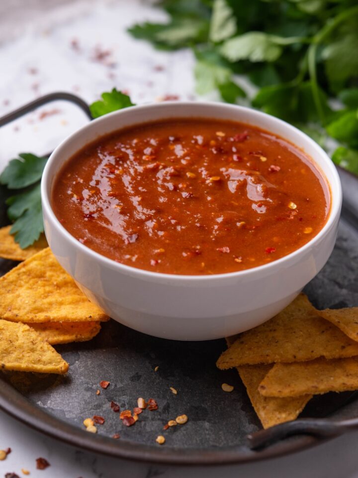 A bowl with chipotle hot salsa on a tray surrounded by tortilla chips.