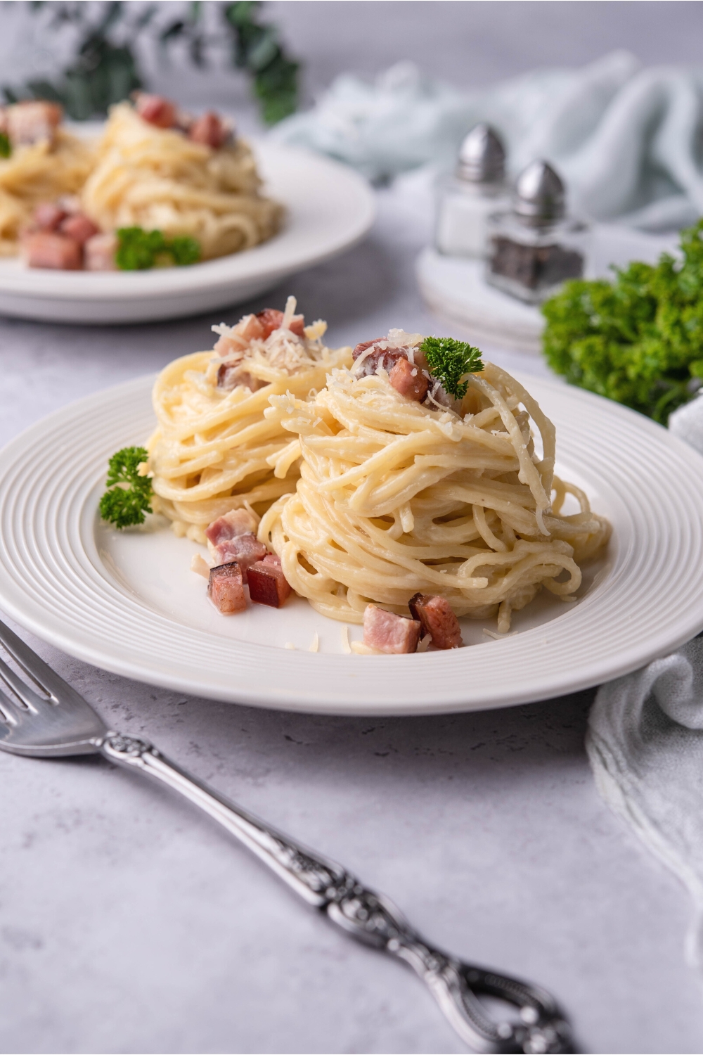 Two stacks of spaghetti noodles with diced pancetta and Parmesan cheese on them on a white plate.
