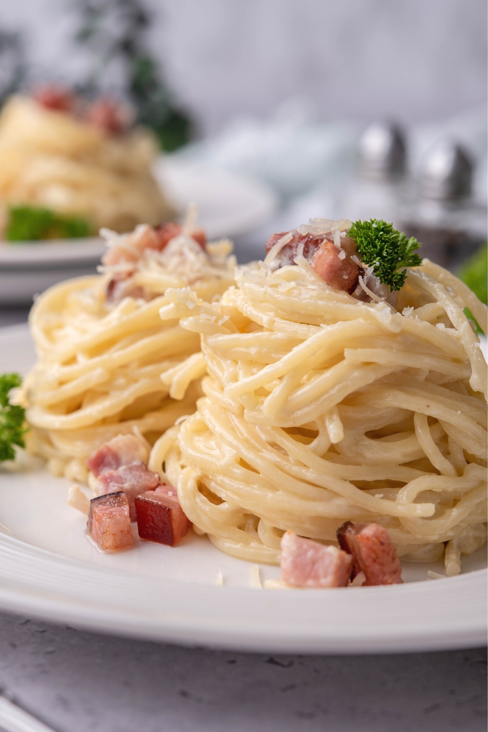 A bundle of spaghetti noodles with pancetta and Parmesan cheese on them with another pile of noodles behind it.