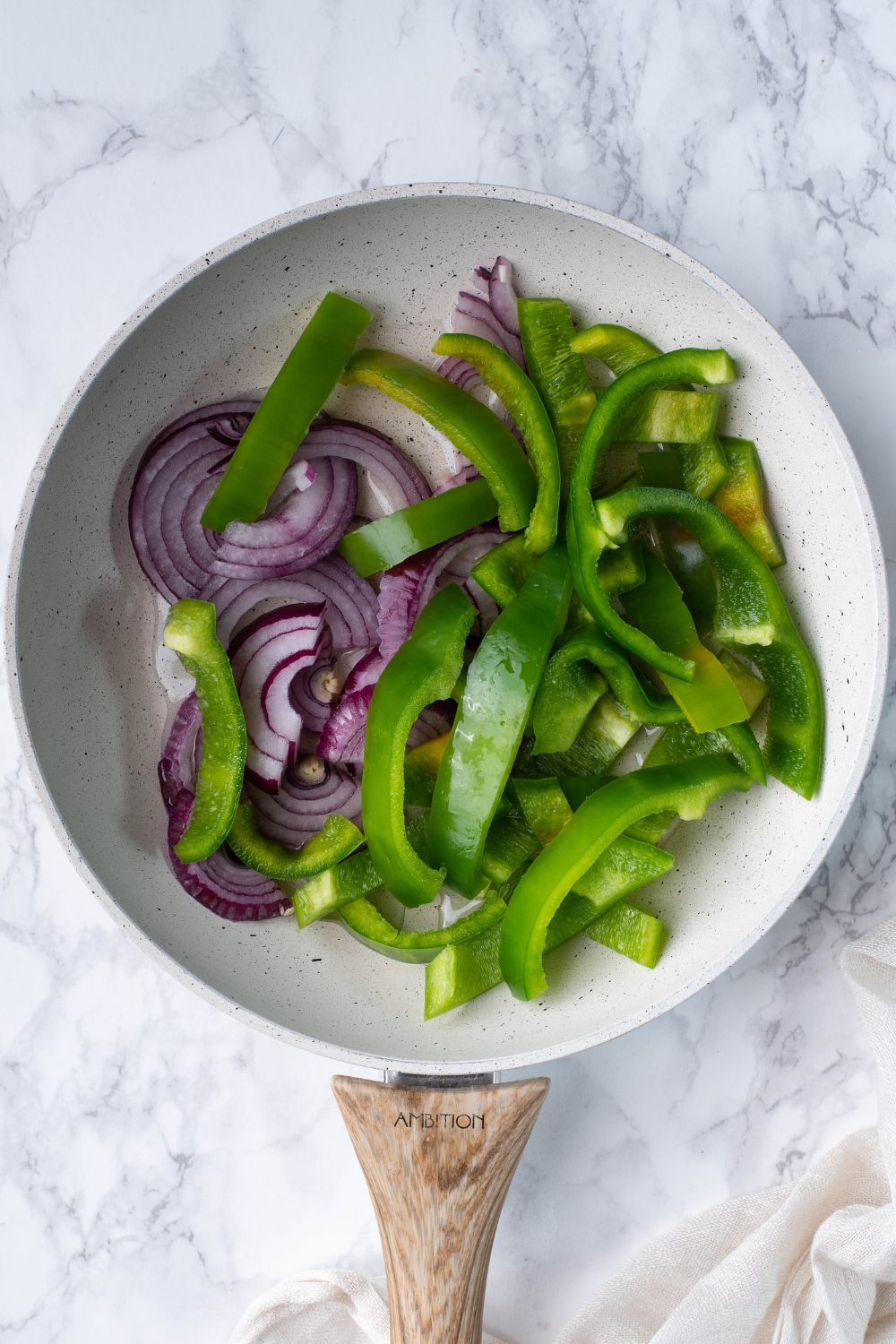 A frying pan with sliced green peppers and onions.