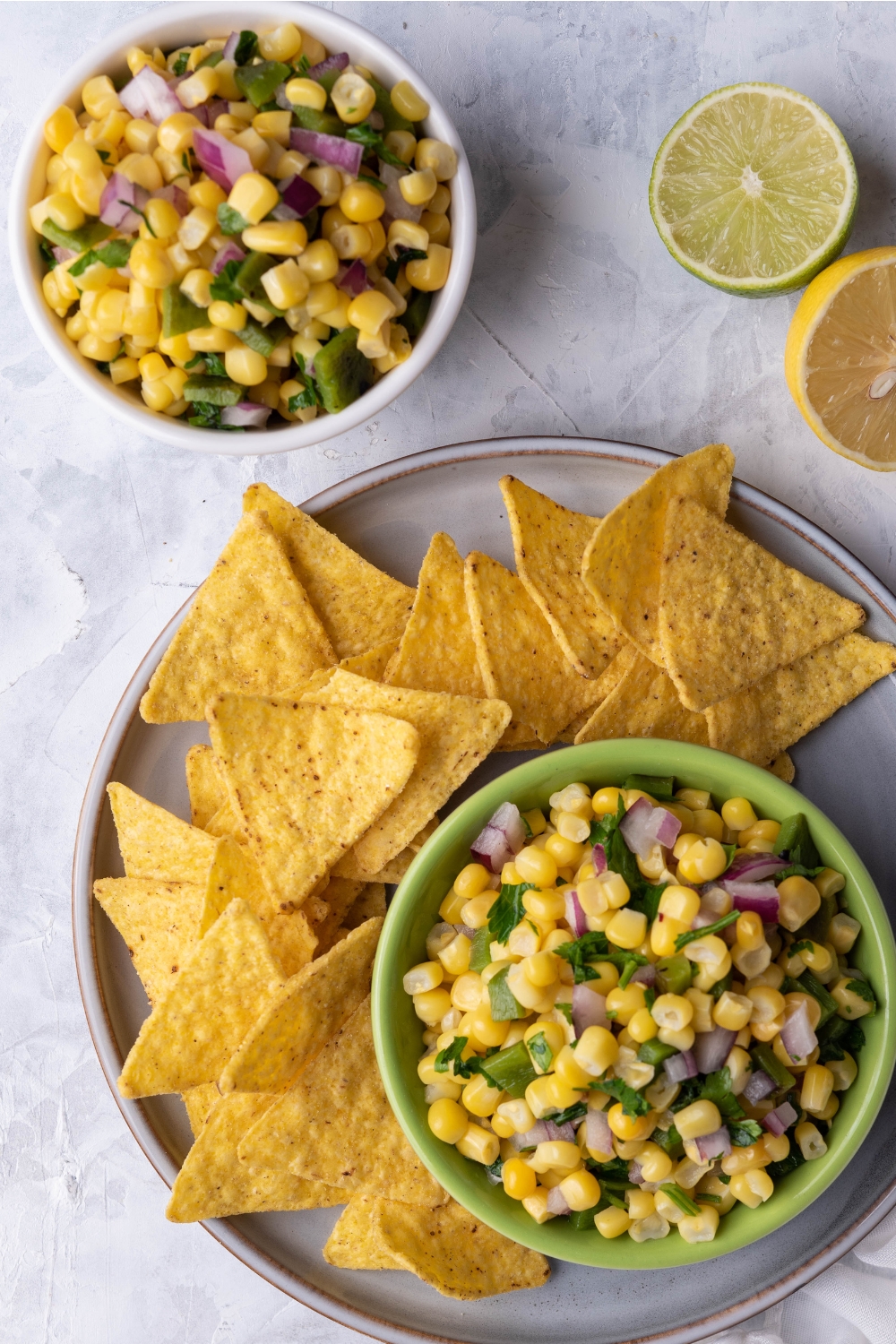 An overhead view of a small dip bowl with corn salsa and tortilla chips on the side of it. A second bowl with corn salsa is next to the serving tray.