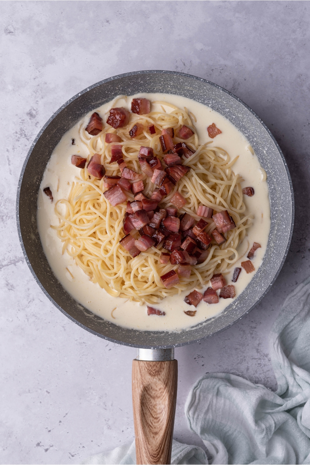 Pancetta on top of spaghetti noodles in a cream sauce in a pan.
