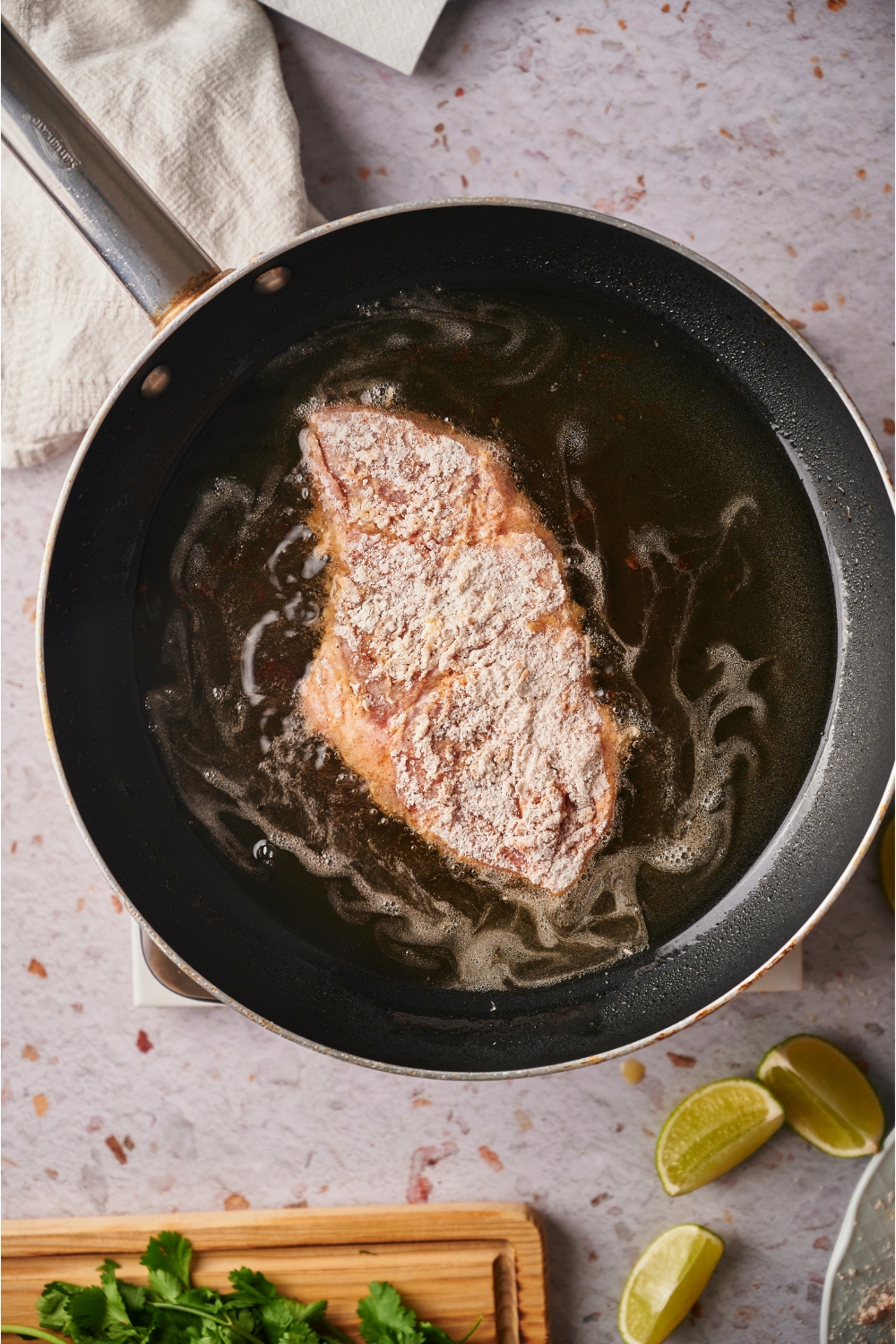 A pork chop coated in flour frying in a pan of oil.