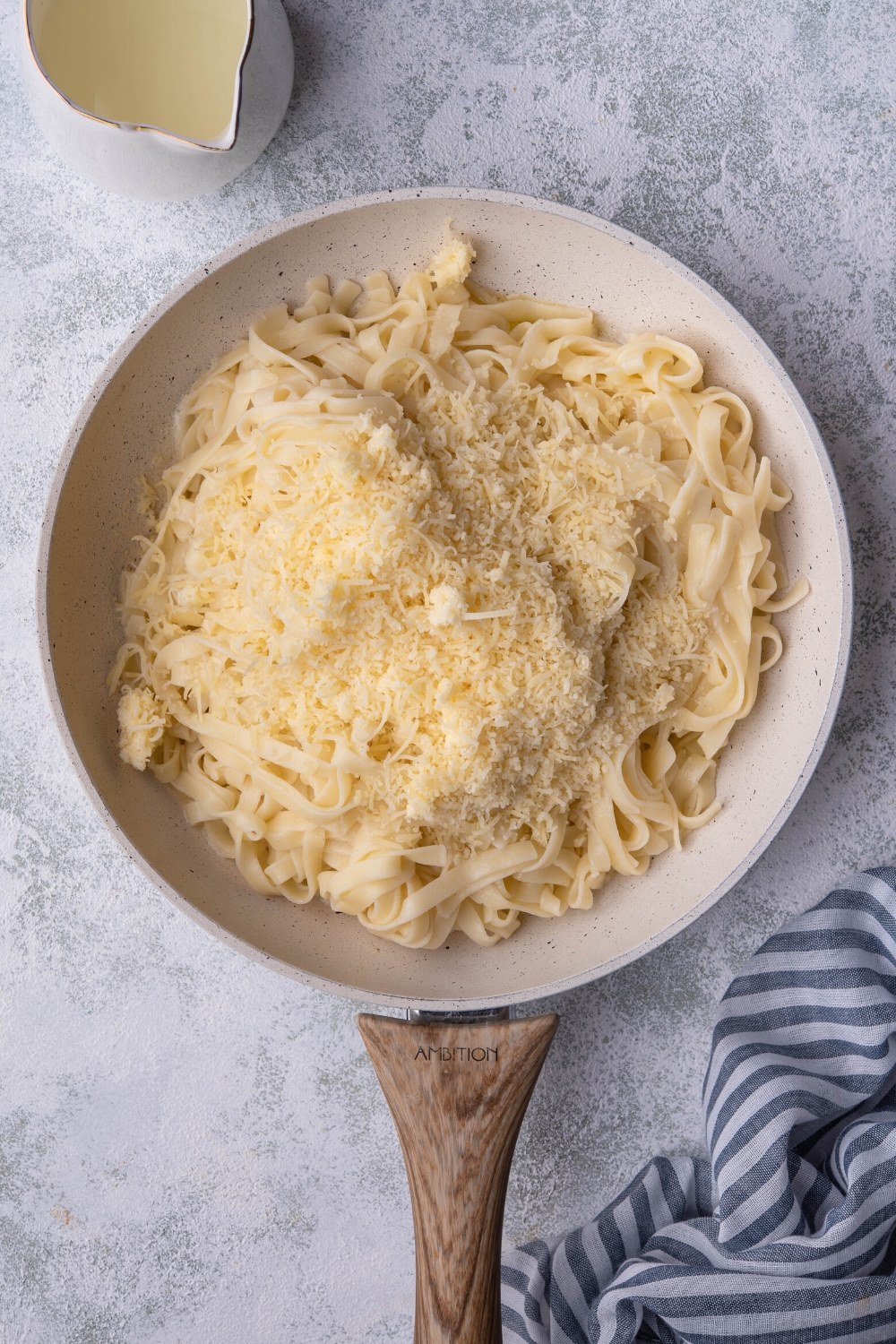 A bunch of parmesan cheese on on top of noodles in a skillet.