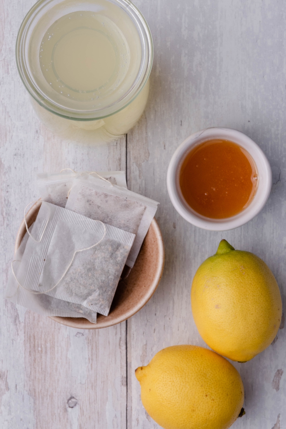 A countertop with a pitcher of lemon water, a bowl with tea bags, a small bowl with honey, and two lemons.