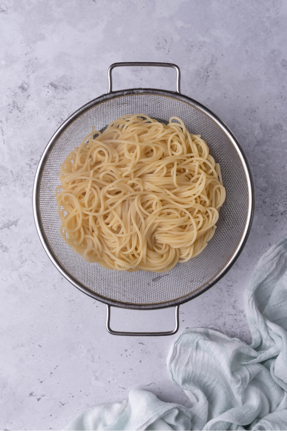 Spaghetti noodles in a mesh strainer.