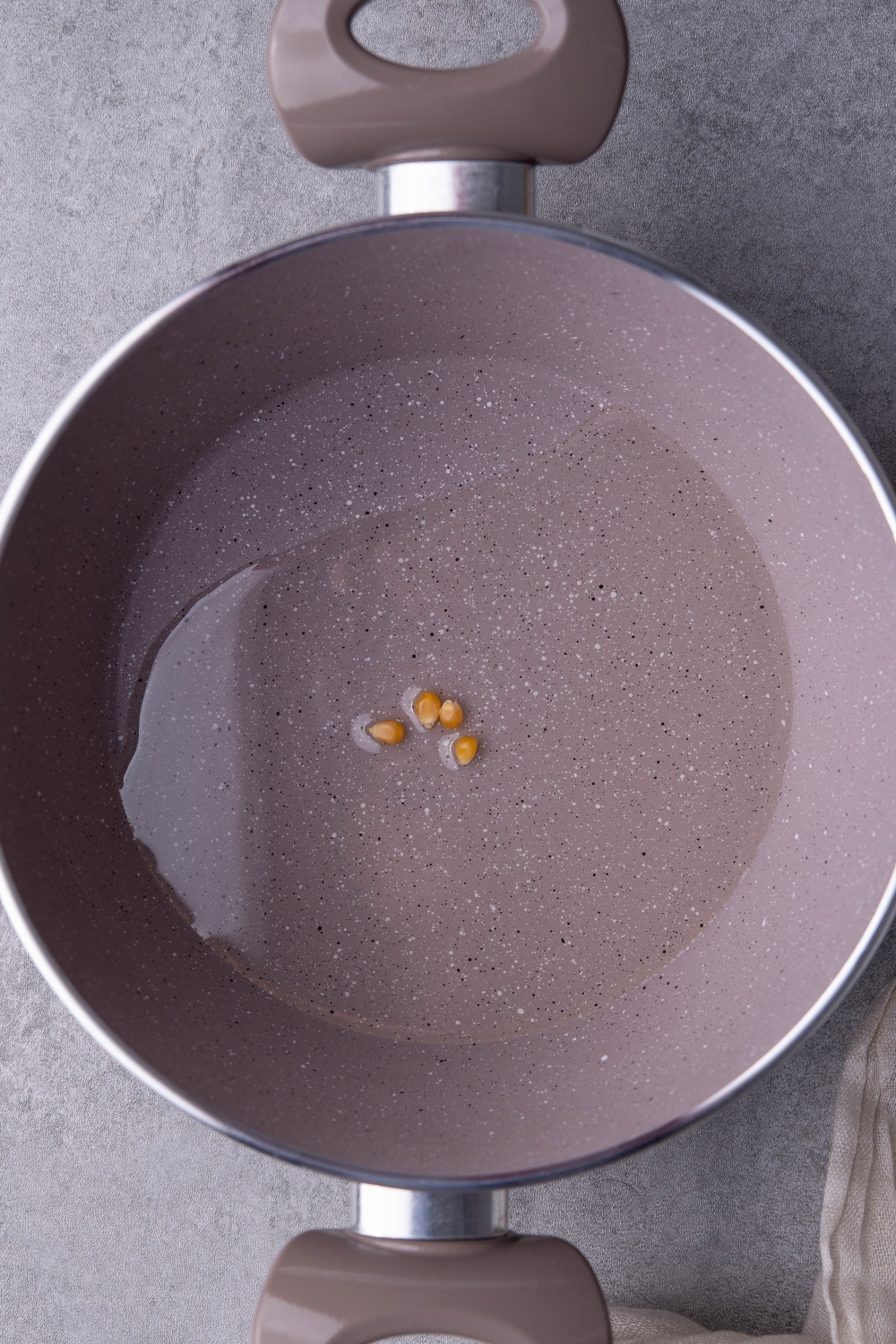 A pot with oil heating four corn kernels.