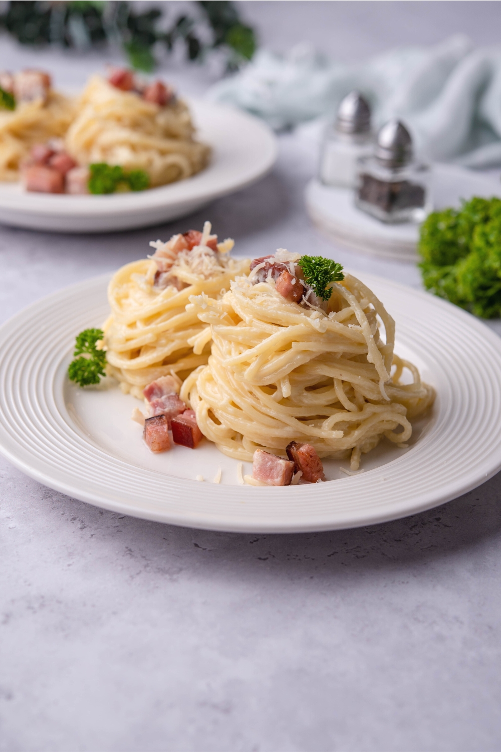 Two bundles of spaghetti noodles with pancetta on them out of white plate.