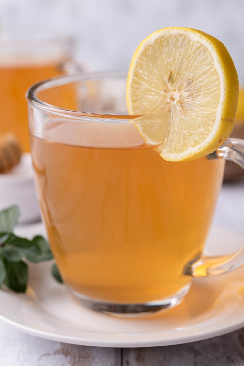 A clear mug with medicine ball tea in it, a slice of lemon is garnished on the side.