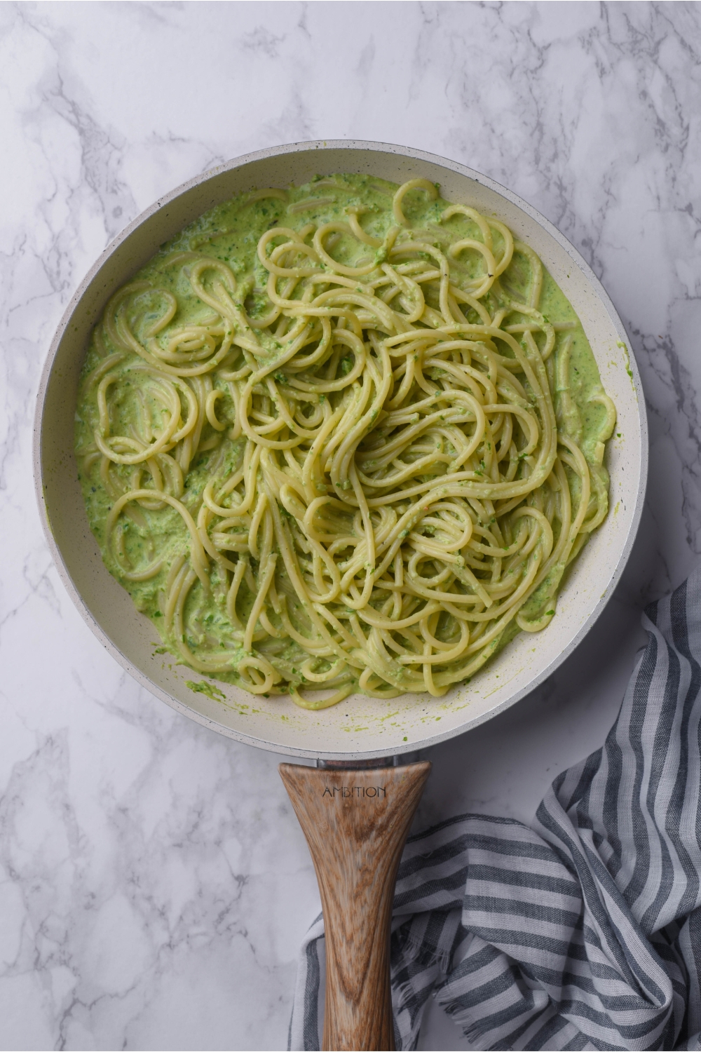 A grey skillet with a wooden handle filled with green spaghetti.