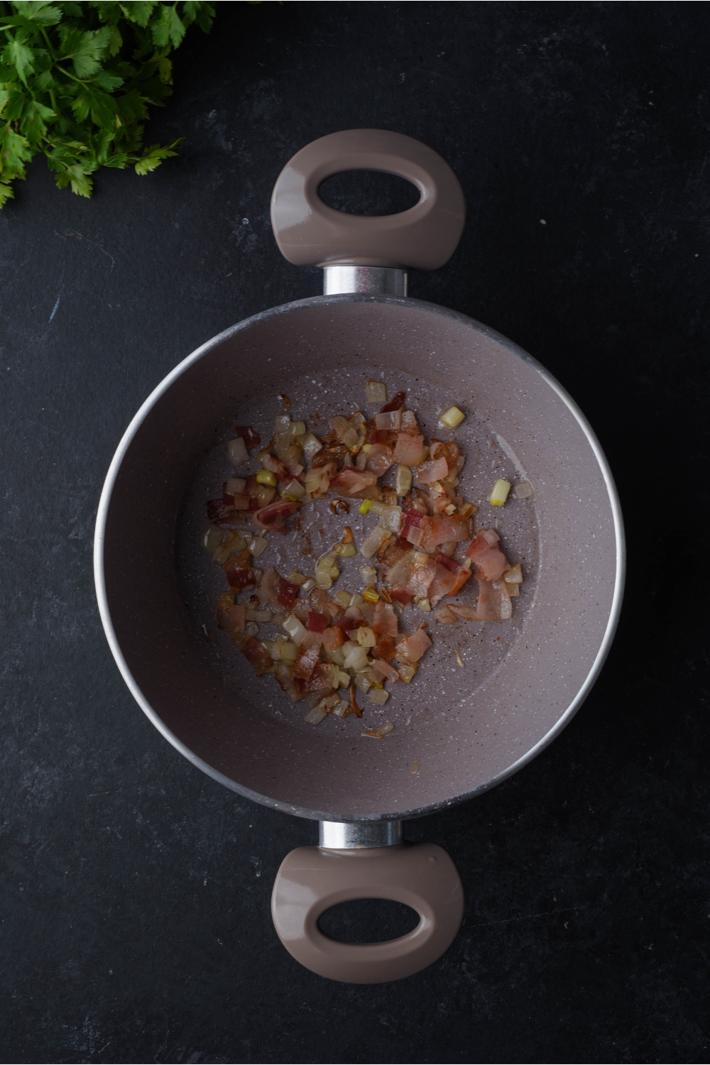 Large grey pot filled with sautéed diced onion and bacon.
