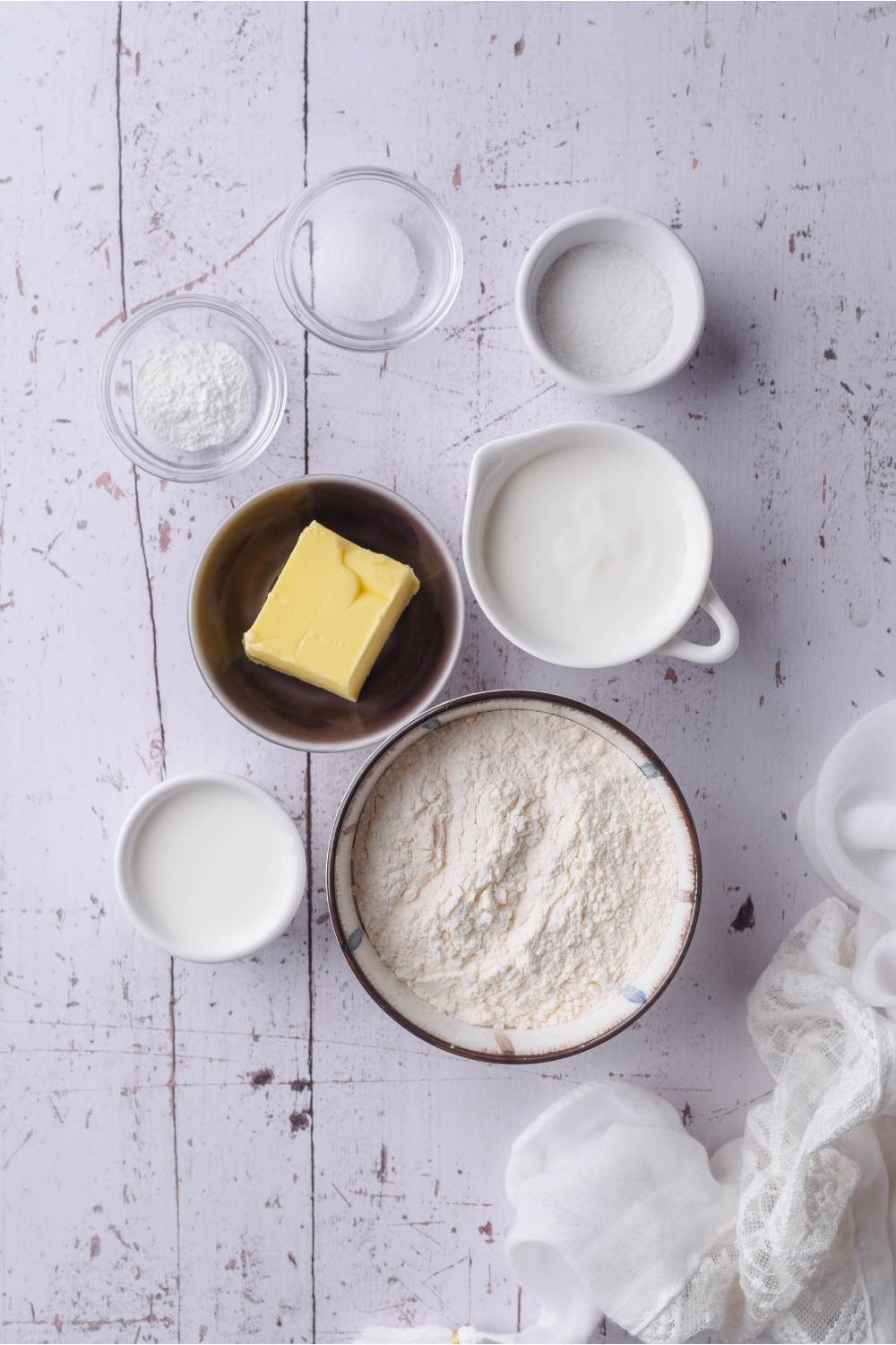 An assortment of ingredients including bowls of flour, buttermilk, milk, butter, and baking powder.