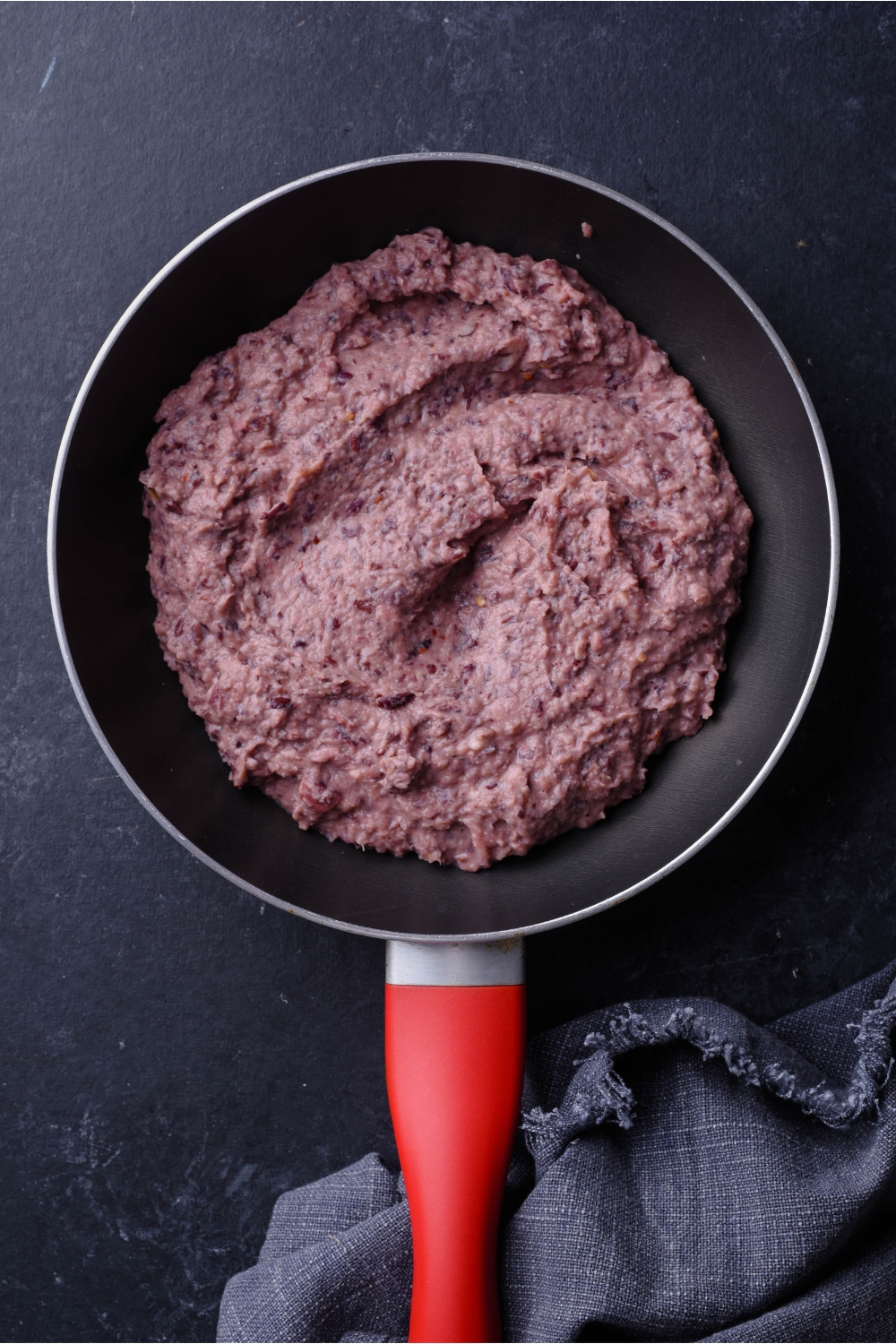 A skillet with a red handle that is filled with a blended bean mixture.