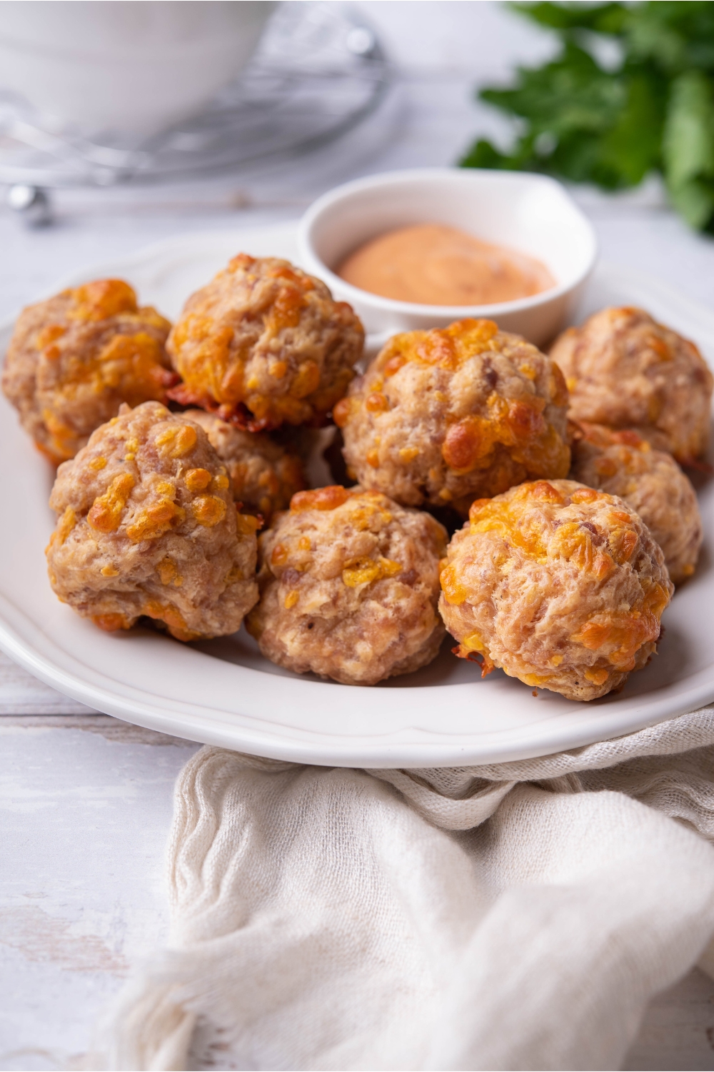 A pile of sausage cream cheese balls on a white plate with a bowl of dipping sauce.