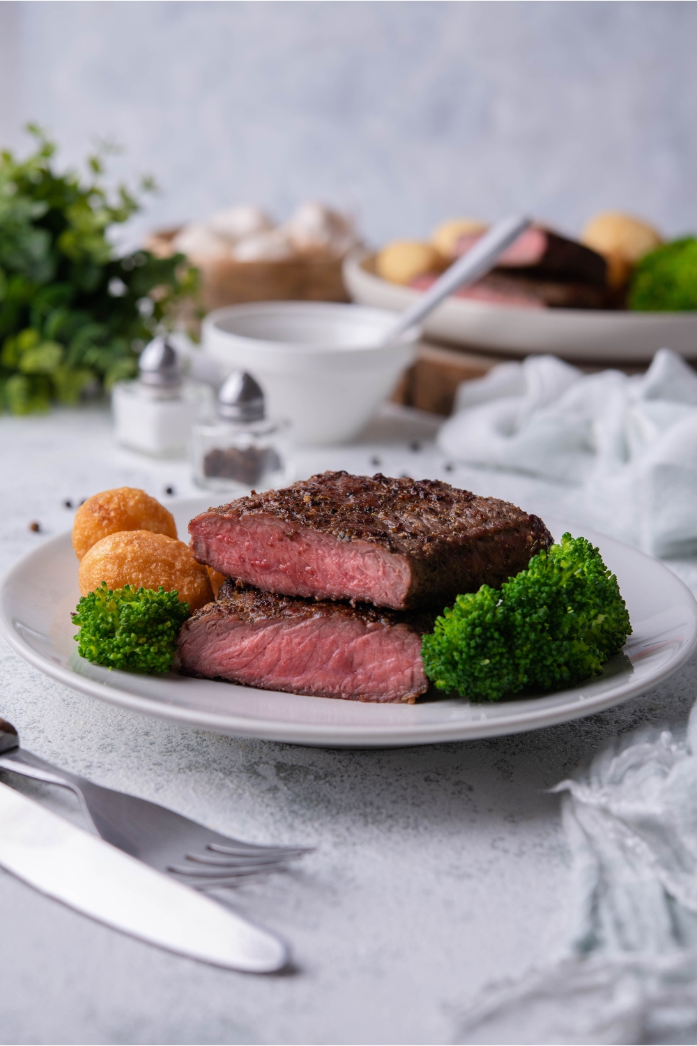 Flat iron steak cut in half with each half stacked on each other, on a white plate with broccoli and nuggets on the plate.