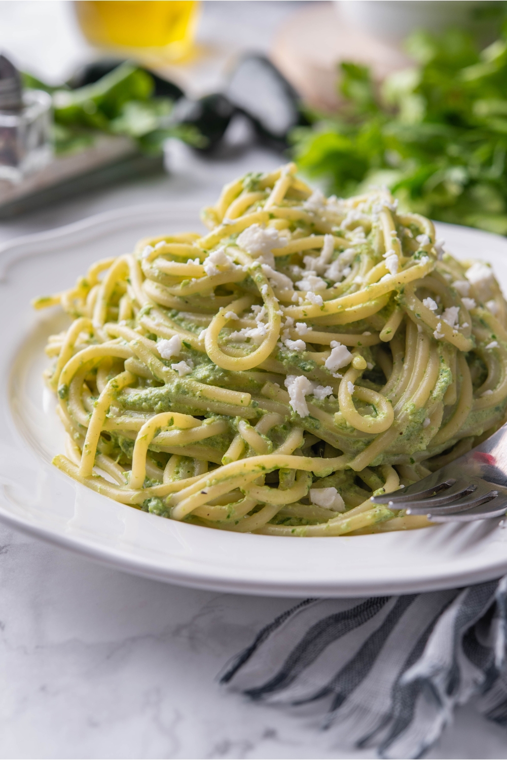 A bed of green spaghetti topped with Cotija on a white plate with a fork on the plate.