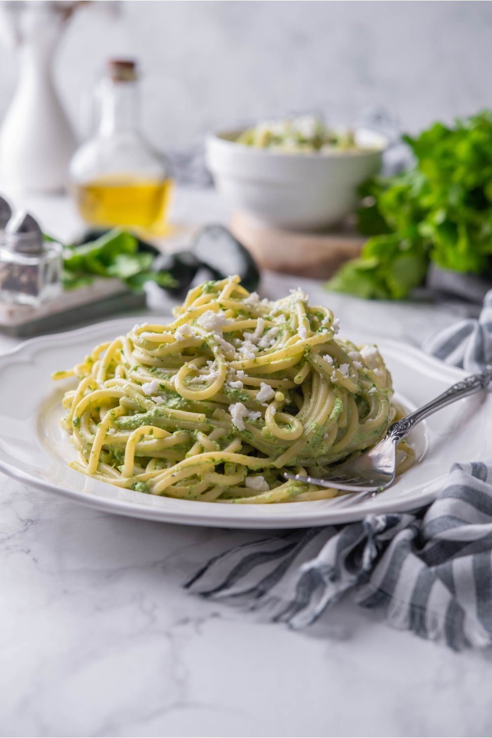 A bed of green spaghetti topped with Cotija on a white plate with a fork on the plate.