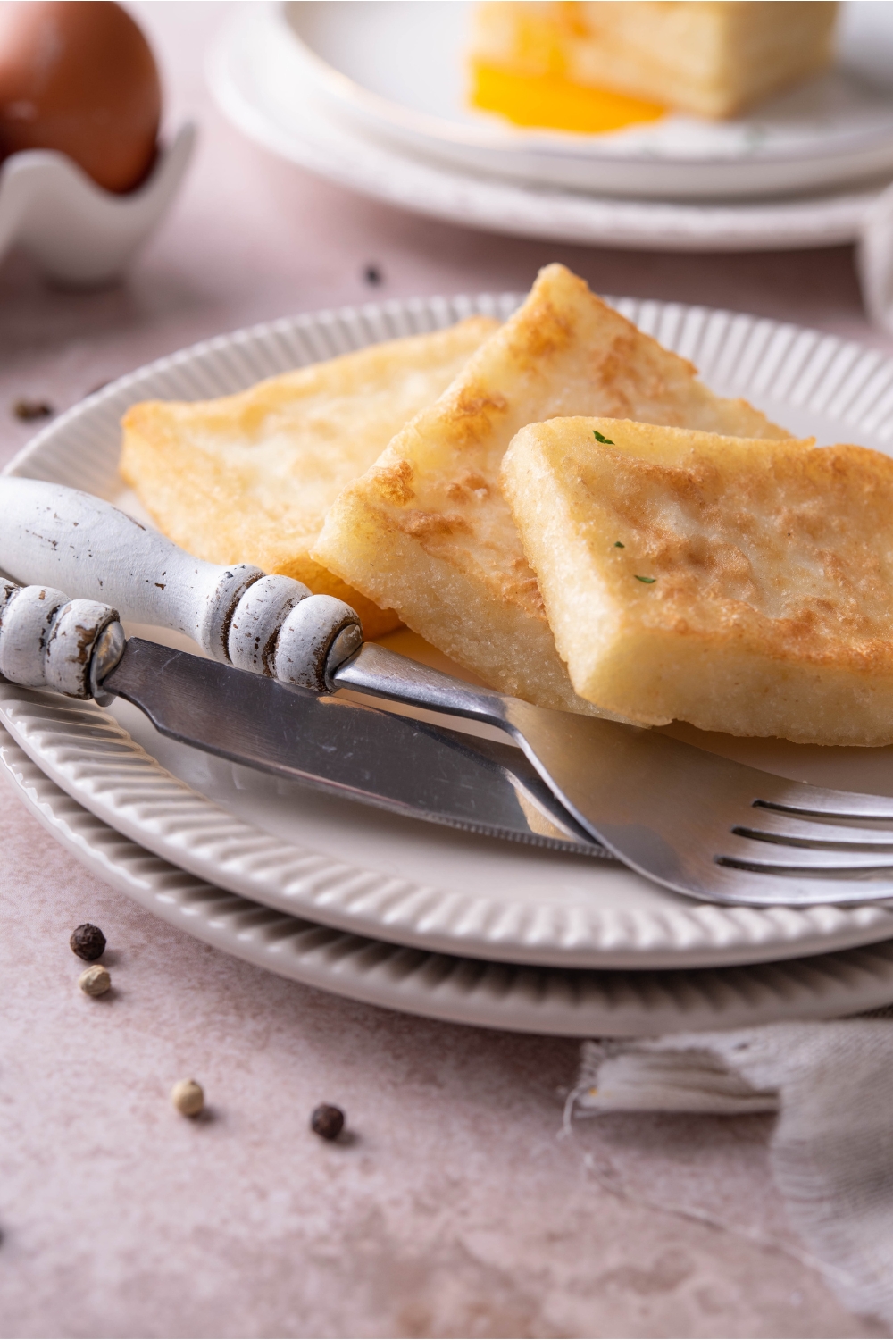 Three grit cakes layered on top of each other on a white plate with a set of silverware on the plate.