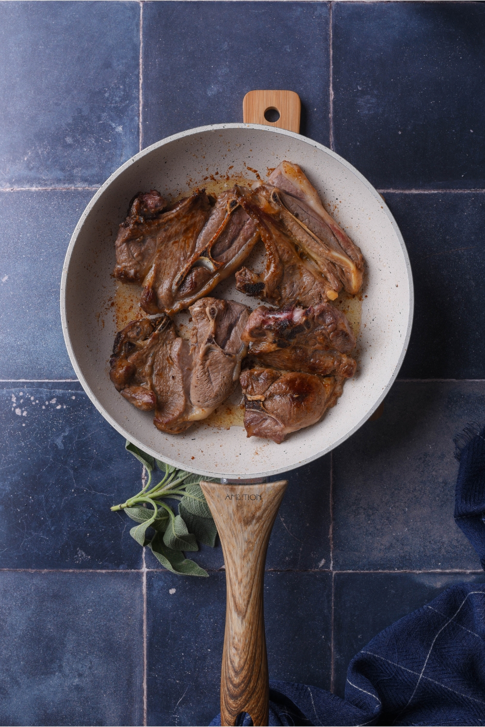 Grey skillet with a wooden handle. The skillet is filled with cooked lamb chops.