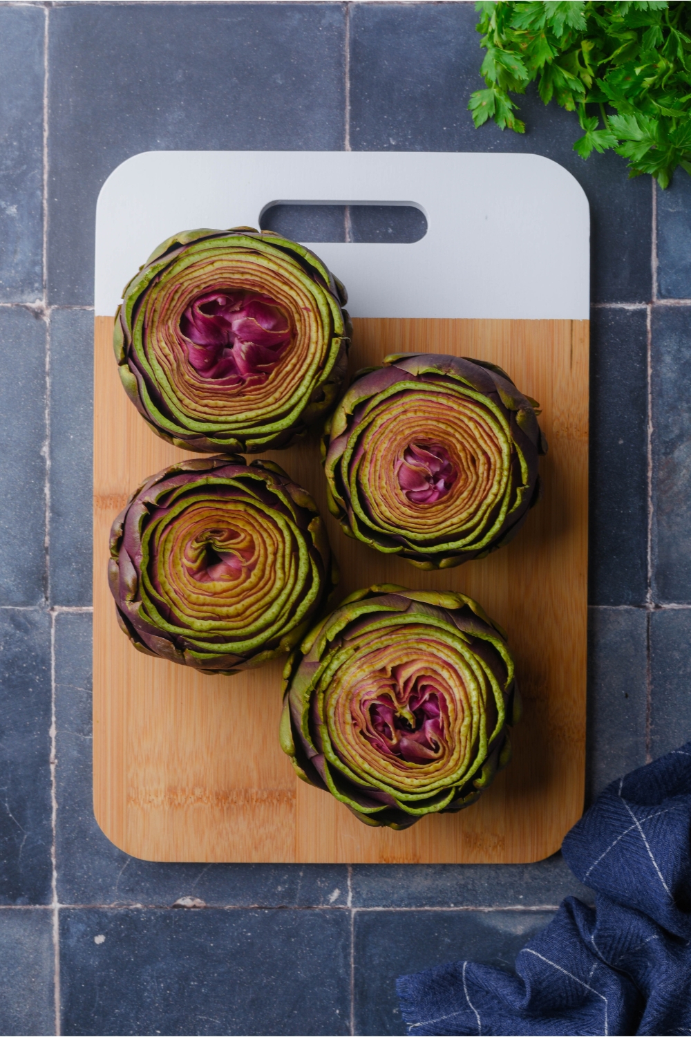 Overhead view of four trimmed whole artichokes on a wooden board.