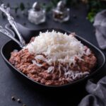 A black serving dish with Popeyes beans and rice in it. There's a set of silverware in the serving dish.