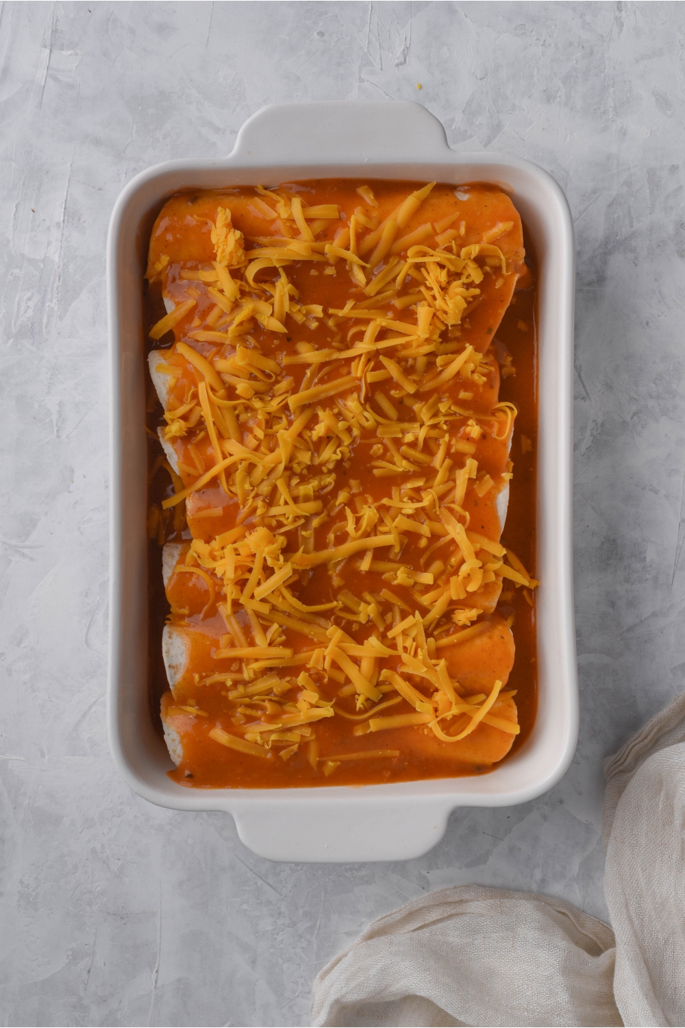 Unbaked cream cheese chicken enchiladas covered in enchilada sauce and shredded cheese.