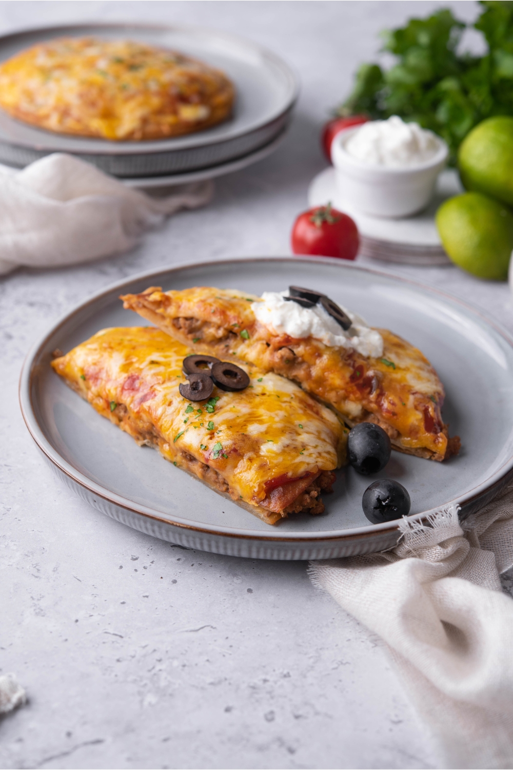 A blue plate with a Taco Bell Mexican pizza that has been cut in half, with one half layered on top of the other. The top slice of pizza is topped with sour cream and black olives.
