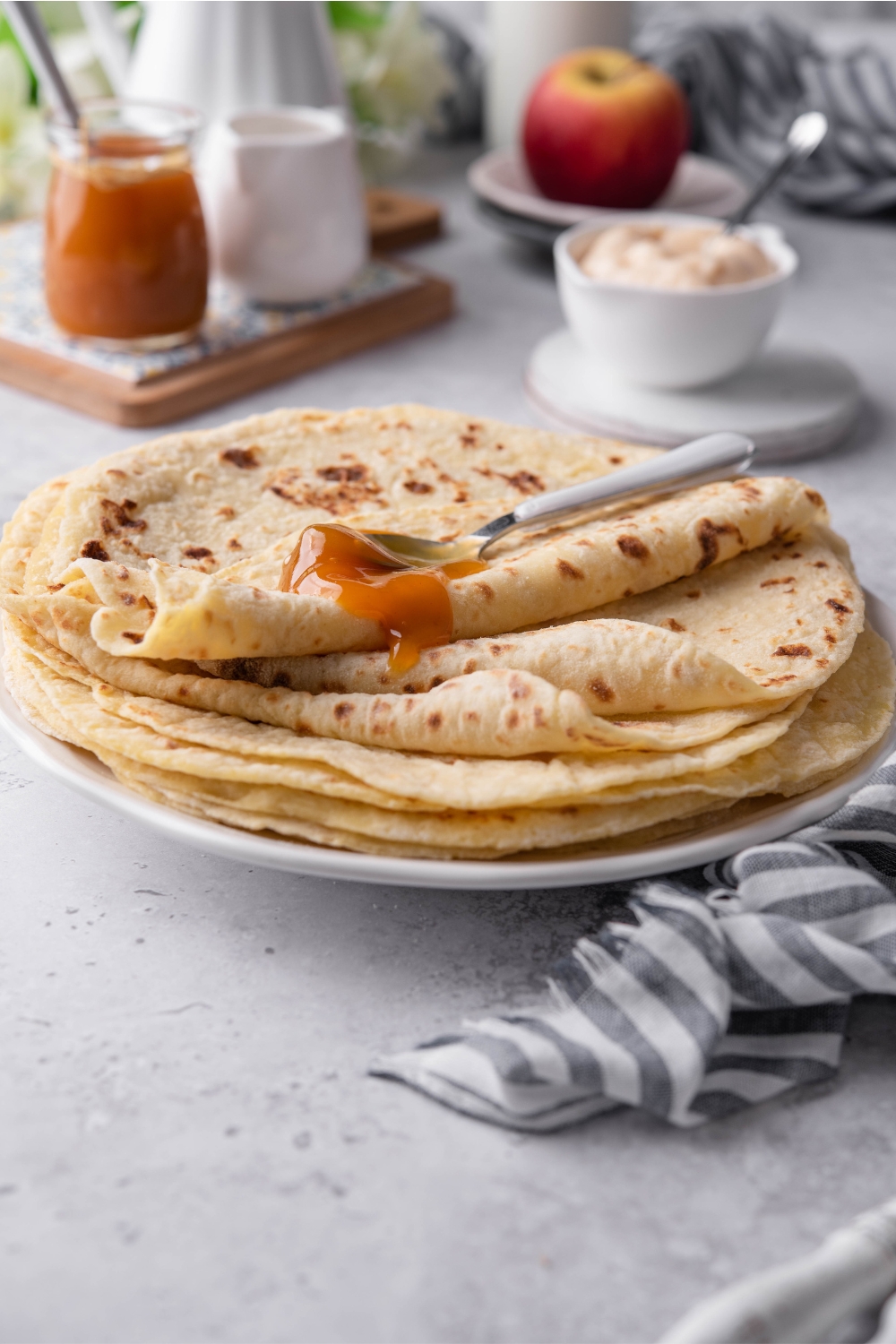 A stack of lefse flatbread with a spoonful of apple butter on top, and some apple butter dripping over the lefse.