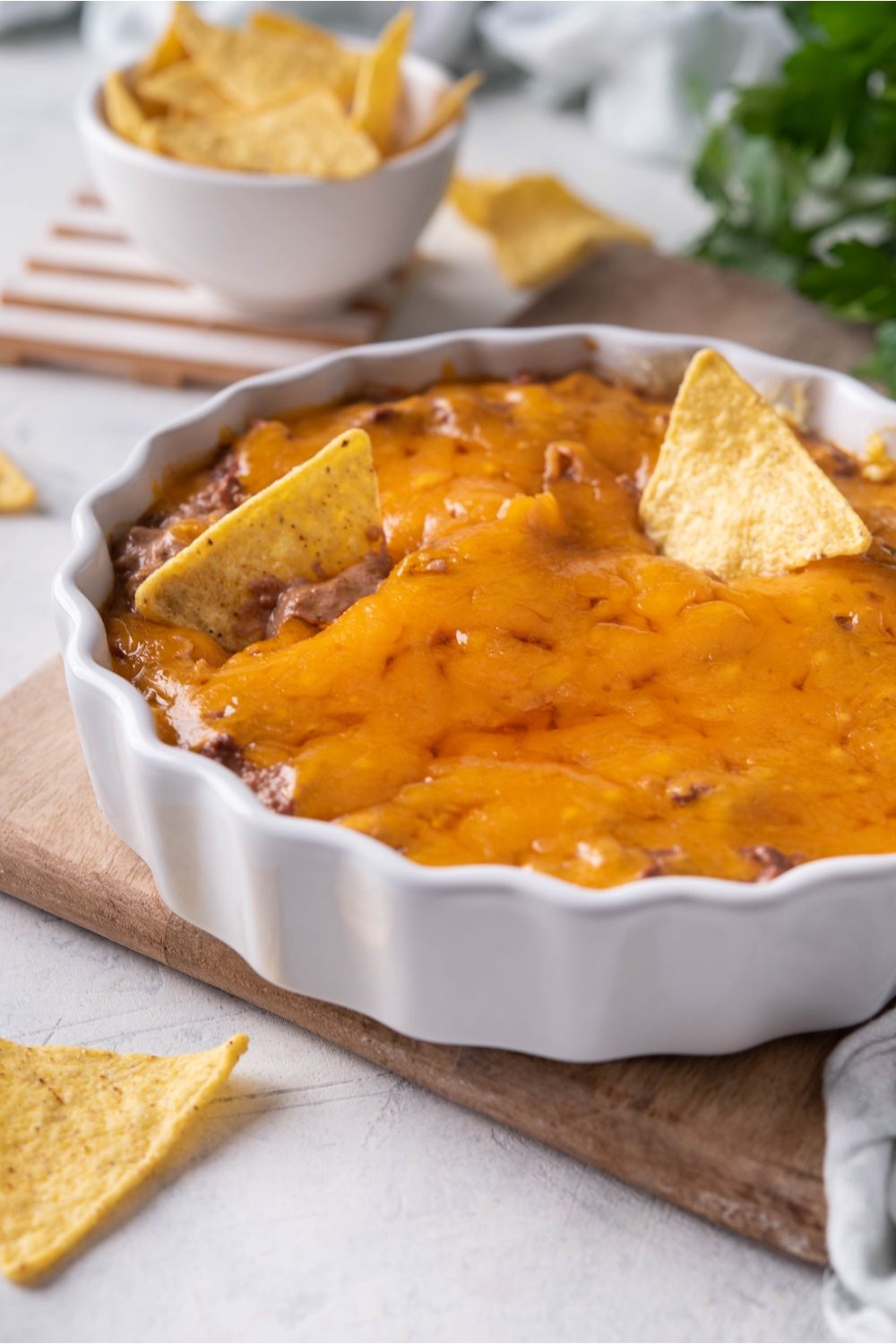 Skyline chili dip in a white serving dish with two tortilla chips sticking out of the dip. The serving dish is on a wood board and there is a bowl of tortilla chips in the background.