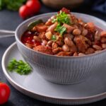 Charro beans in a blue bowl atop a blue plate, garnished with fresh herbs.