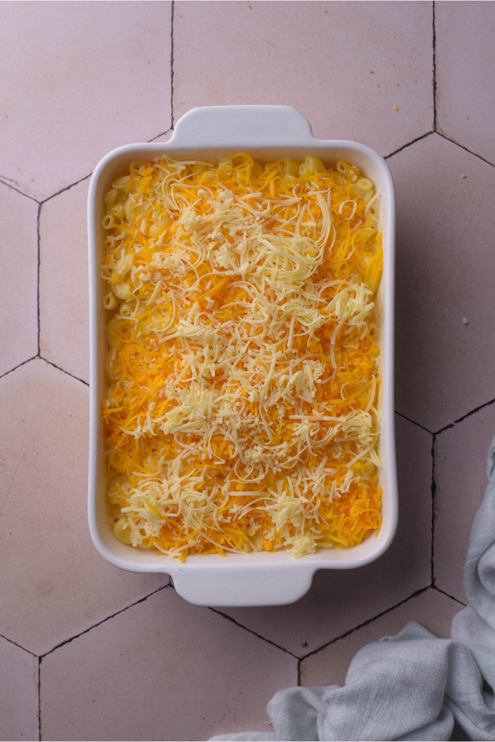 A white baking dish filled with unbaked mac and cheese covered in a layer of unmelted shredded cheese.