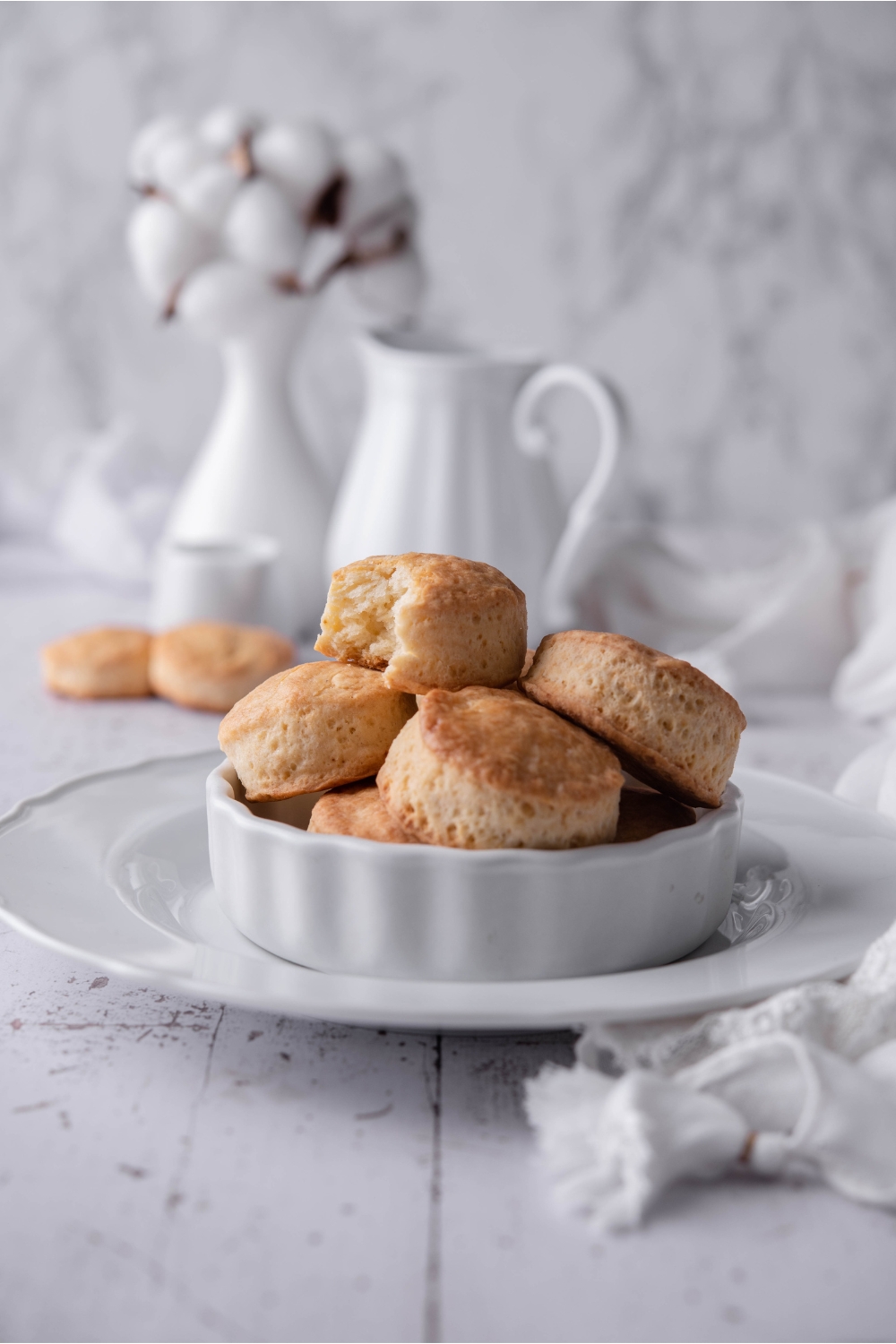 A white dish atop a white serving tray with a pile of Popeye's biscuits in the dish. There's a bite taken out of one of the biscuits on top of the pile.
