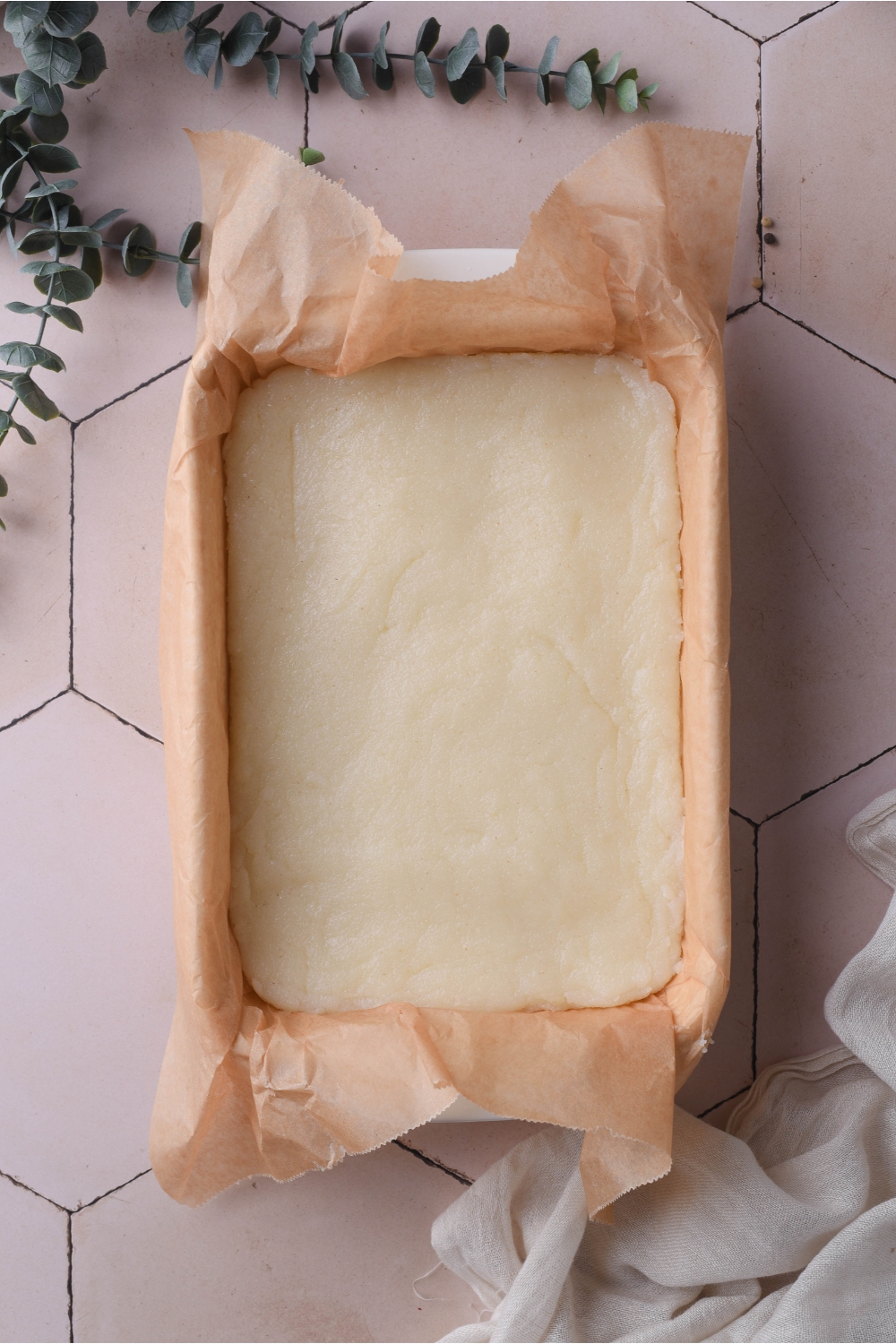 Cooked and cooled grits in a baking dish lined with parchment paper. The parchment paper is hanging off the edges of the baking dish.